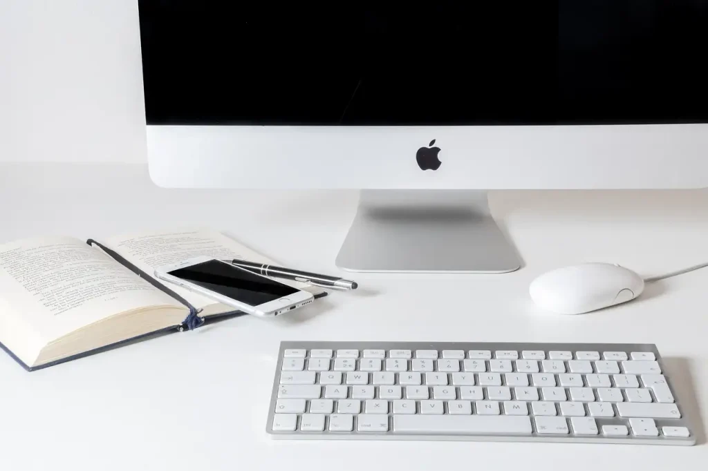 白いデスクにiMac、キーボード、本とスマートフォンが置かれている